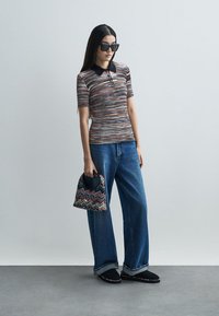 Sweter polo z kolorowym wzorem, czarnym kołnierzykiem, zestawiony z luźnymi niebieskimi dżinsami, czarnymi butami na płaskiej podeszwie i torebką w wzory.