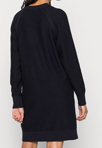 Robe pull en maille bleu marine avec manches longues, poignets et ourlet côtelés. Présente des coutures détaillées le long des coutures des épaules. Texture douce.