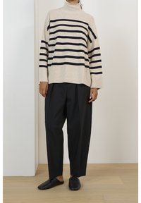 Béžový rolák s černými horizontálními pruhy, doplněný černými širokými kalhotami a černými slip-on botami; hladká textura.