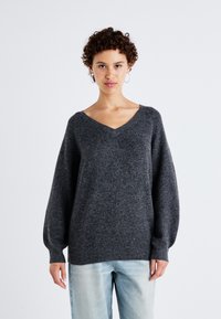 Maglione grigio scuro a scollo a V con maniche lunghe e a palloncino, realizzato in un materiale morbido e testurizzato, abbinato a jeans azzurri chiari.