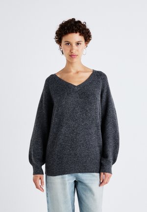 Pull en V gris foncé à manches longues et bouffantes, fabriqué dans un matériau texturé doux, associé à un jean bleu clair.