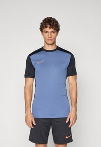 Nike idretts skjorte med blå kropp og svarte ermer, rund hals, og gull logo på venstre bryst, sammen med mørke shorts.