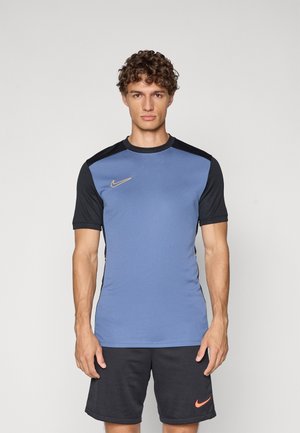 Nike træningsshirt med en blå krop og sorte ærmer, rund hals, og et gyldent logo på venstre bryst, kombineret med mørke shorts.