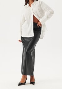 Witte overhemden met een relaxte pasvorm, gecombineerd met een zwarte neplederen kokerrok, geaccentueerd door zwarte pointy heels. Soepele texturen.