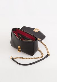 Bolso de cuero negro con una cadena dorada, interior forrado en rojo, cierre de cremallera y un distintivo detalle de broche dorado.