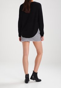 Schwarzer Pullover mit langen Ärmeln, lässig geschnitten, kombiniert mit einem kurzen karierten Rock, der einen lässigen Stil unterstreicht. Schwarze Stiefeletten runden den Look ab.