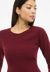 Burgundiapunane soonikkoega kampsun, millel on pikad varrukad ja ümar kaelus. Pehme tekstuur, keha järgnev lõige ja tagasihoidlik kudumismuster.