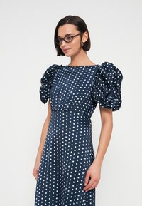 Robe bleu marine avec de grandes manches bouffantes, ornée d'un motif de pois blancs, texture lisse, corsage ajusté et jupe fluide.