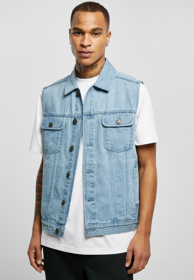 Vest din denim de culoare albastră deschisă, cu guler, închidere prin butoane pe față și două buzunare pe piept. Stilizat peste un maieu alb, cu un croi simplu.