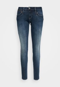 Tummansiniset slim-fit farkut, joissa on hieman haalistumia reisissä, napitus, sekä etu- ja takataskut, asetettu litteäksi valkoiselle taustalle.