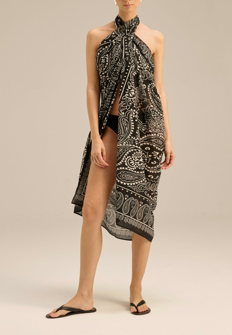 Sukienka sarong w czarno-białym wzorze paisley, lekki materiał, trójkątny kształt z wiązanym dekoltem, noszona na kostium kąpielowy, długość do kostek.