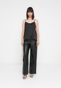 Débardeur en satin noir avec un col orné de sequins, associé à un pantalon large en simili cuir noir taille haute. Accessoirisé avec un sac à main rose.