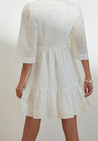 Vestido blanco de manga corta con tejido de ojales, escote redondo y dobladillo con volantes. Cuenta con una cintura ajustable con cordón para un ajuste personalizado.