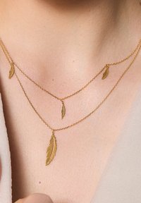 Złota naszyjnik warstwowy z delikatnymi zawieszkami w kształcie piór, różniącymi się rozmiarem i detalami, z cienkimi ogniwami łańcuszka i wypolerowanym wykończeniem.