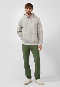 Jasnoszara, teksturowana bluza z kapturem, przednią kieszenią, sznurkiem do ściągania kaptura oraz kremowymi, prążkowanymi mankietami. Połączona z zielonymi spodniami i białymi tenisówkami.