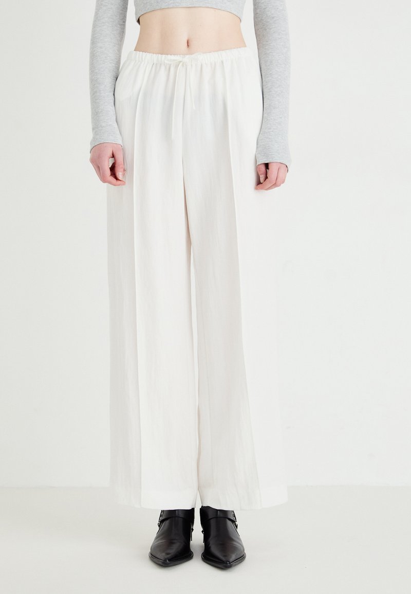 White wide-leg trousers with an elastic waistband, made of lightweight fabric; paired with fitted gray long sleeves and black ankle boots.