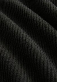 Tessuto nero a coste con una superficie morbida e texture, caratterizzato da linee ondulate che creano profondità e contrasto nel materiale.