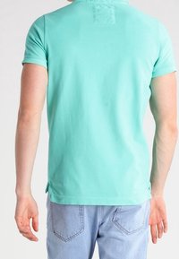 T-shirt azzurro chiaro a maniche corte con scollatura rotonda e spacchi laterali; abbinato a jeans in denim blu chiaro con dettagli di cucitura in evidenza.