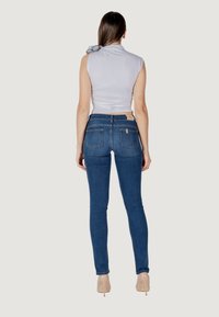 Jeans skinny blu con vita alta, cinque tasche e un'etichetta beige sul retro. Abbinati a un top grigio aderente con un dettaglio a fiocco sulla spalla.