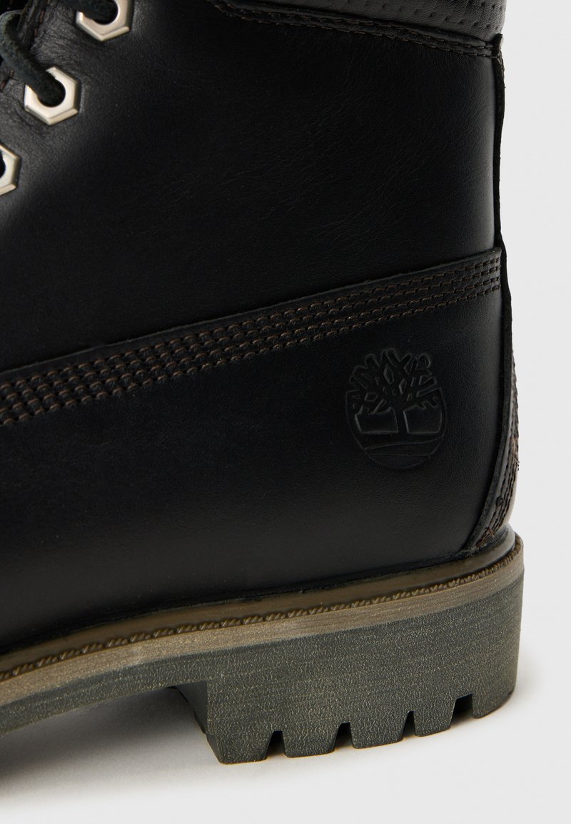 Schwarzer Lederstiefel mit geprägtem Baum-Logo, detaillierter Naht, metallischen Schnürsenkel-Ösen und robustem grauem Gummisohle mit tiefen Profilen.