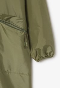 Giubbotto leggero verde oliva con tasca anteriore con zip, polsini arr gathered e logo Lacoste sul tirante della zip e sul tessuto.