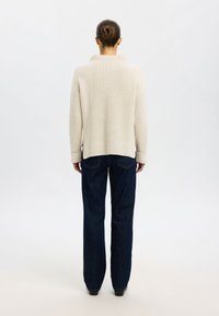 Pull en tricot côtelé crème avec un col montant, associé à un jean bleu foncé à jambes larges. Texture douce et design décontracté.