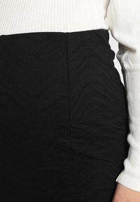 Zwarte gestructureerde rok met golvende patronen, gemaakt van rekbaar materiaal. Gecombineerd met een witte geribbelde top, die contrasterende kleuren laat zien.