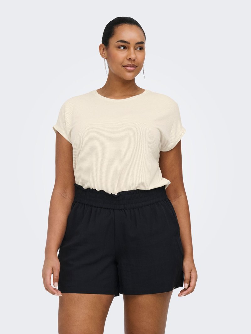 Femme portant un haut crème à manches courtes et un short noir à taille élastique, debout avec les bras détendus devant un fond clair uni.