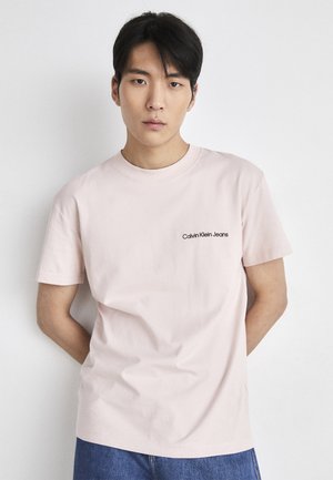 T-shirt di cotone rosa chiaro con maniche corte e colletto a girocollo, con un piccolo logo nero "Calvin Klein Jeans" sul petto sinistro.
