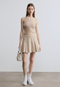 Camiseta sin mangas beige con diseño acanalado, combinada con una falda beige plisada y zapatillas blancas. Accesorios con un bolso pequeño.