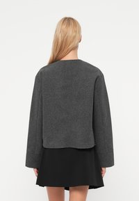 Γκρι σακάκι από μείγμα μαλλιού με ευθεία κοπή, χαμηλωμένους ώμους και μακριά μανίκια. Διαθέτει μινιμαλιστικό σχέδιο και διακριτή υφή.