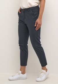 Mörkblå chinos i bomull med slim fit. Har sidofickor, knappstängning framtill och fållade ärmar. Bärs med vita sneakers.