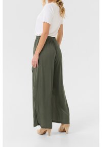 Pantaloni ampi color verde oliva con vita elasticizzata, realizzati in tessuto leggero. Abbinati a un top bianco con scollatura a onde.