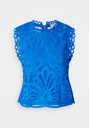 Top in pizzo blu con motivi floreali intagliati, maniche scallop e un design a collo alto. Dettaglio con zip sul retro per la chiusura.