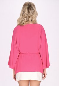 Roza kimono-slogna majica s širokimi rokavi, pasom in lahkim materialom, ki se lepo spusta. Nositi jo je mogoče čez belo oblačilo.