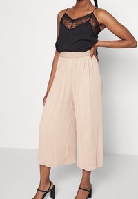 Svart satin cami med spetsdetaljer, ihopparad med veckade ljusbeige culottes. Smala svarta axelremmar och texturerad midjebanddetalj.