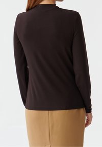 Langärmliges schwarzes Oberteil aus glattem Stoff, mit hohem Kragen und lockerer Passform, kombiniert mit beigen, tapered Hosen.