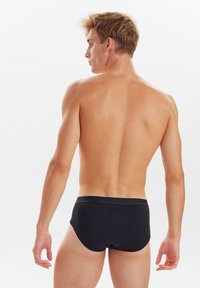 Sorte svømmebukser med en glat tekstur og en behagelig elastisk talje, designet til en tætsiddende pasform. Bagsidevisningen viser minimal dækning.