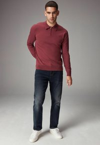 Bordeaux zip-up pullover med krave, båret med mørkeblå jeans og hvide sneakers. Glat tekstur, tætsiddende design og minimal dekoration.