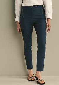 Námořnické slim-fit kalhoty s dvěma zipovými předními kapsami, úzkým střihem, strukturovanou tkaninou a malým rozparkem na lemu, doplněné černými páskovými botami.