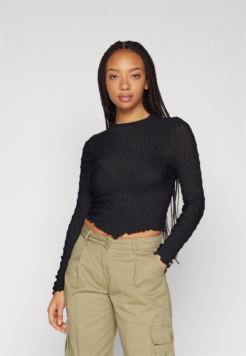Svart langermet crop topp med en teksturert, samlet design og bølget kant, kombinert med khaki høytlivs cargo bukser.