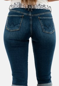 Jeans in denim blu scuro con una vestibilità a vita media, dotati di una cintura bianca con motivo e tasche posteriori distintive con dettagli cuciti.