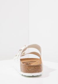 Weiße Sandale mit einem Korkfußbett, zwei verstellbaren Riemen und einer goldfarbenen Schnalle. Die strukturierte Oberfläche sorgt für Grip und Komfort.