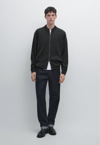 Veste bomber zippée grise foncée avec un col, portée sur un T-shirt blanc, associée à un jean droit en denim foncé et des bottes noires.