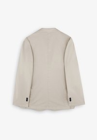 Blazer beige con una silueta ajustada, mangas largas y dos botones negros en cada puño. Tejido suave con un ligero brillo.