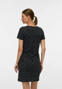 Črna obleka iz mehkega blaga, ki ima oprijet kroj in kratke rokave. Okrašena je z malimi rosa srčkastimi vzorci po celotnem oblačilu.