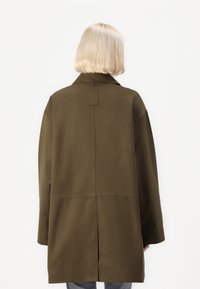 Olivenfarget frakk med avslappet passform, stor krage og detalj med spaltet bak. Laget av lett stoff, med et rent, minimalistisk design.