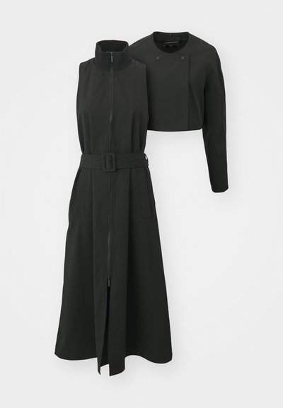 Black sleeveless dress with a high collar, front zipper, belted waist, and a cropped jacket with two buttons and long sleeves.