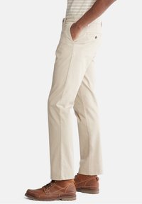 Beige chinos med rak bendesign, i bomullstyg, sidofickor och en bakficka med knappstängning, matchade med bruna läderstövlar.