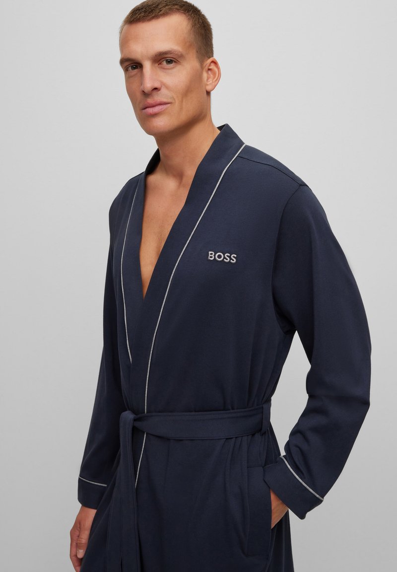 Marine badjas van zacht materiaal, met witte bies, een strik aan de voorkant en een logo op de borst. Beschikt over lange mouwen en zijzakken.